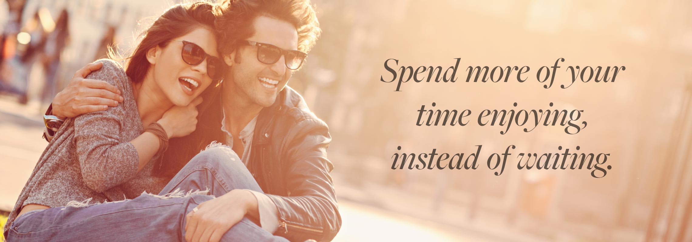 Happy, young couple enjoying the outdoors in the sun, wearing glasses that have photochromic lenses that get darker in the sunlight with the statement on the image; Spend more of your time enjoying, instead of waiting.