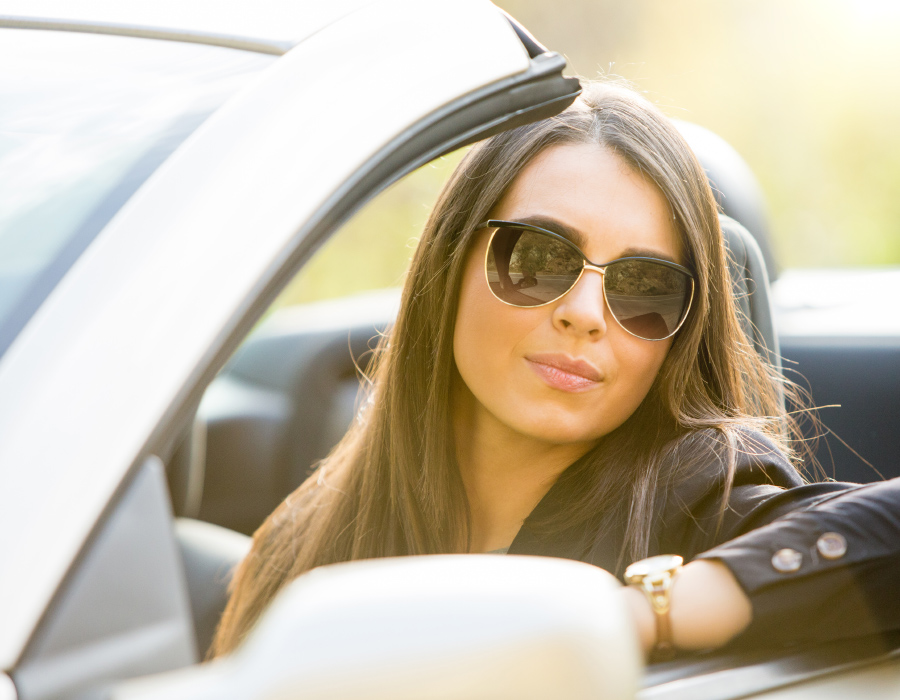 Woman sitting in a convertible car wearing glasses that have photochromic lenses that get darker in sunlight